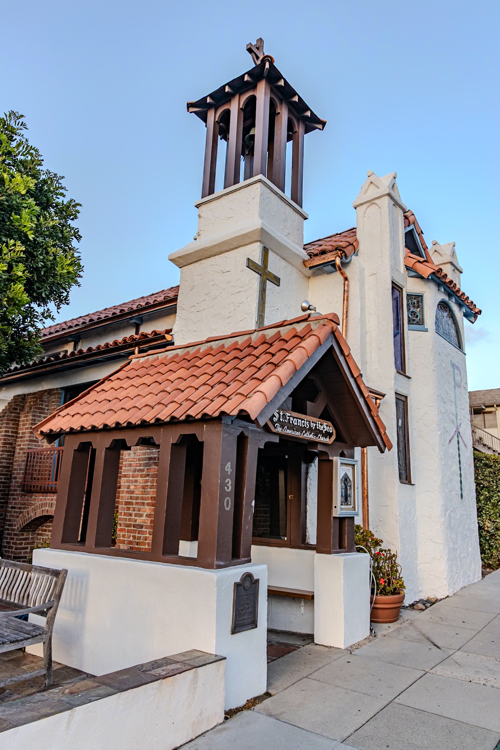 Front of St. Francis by-the-Sea on Park Avenue: a white stucco church with an open wooden bell tower and cross, red tile roofs and a tiled entry porch with the sign "St. Francis by the Sea, The American Catholic Church", the number 430 and a National Register plaque.